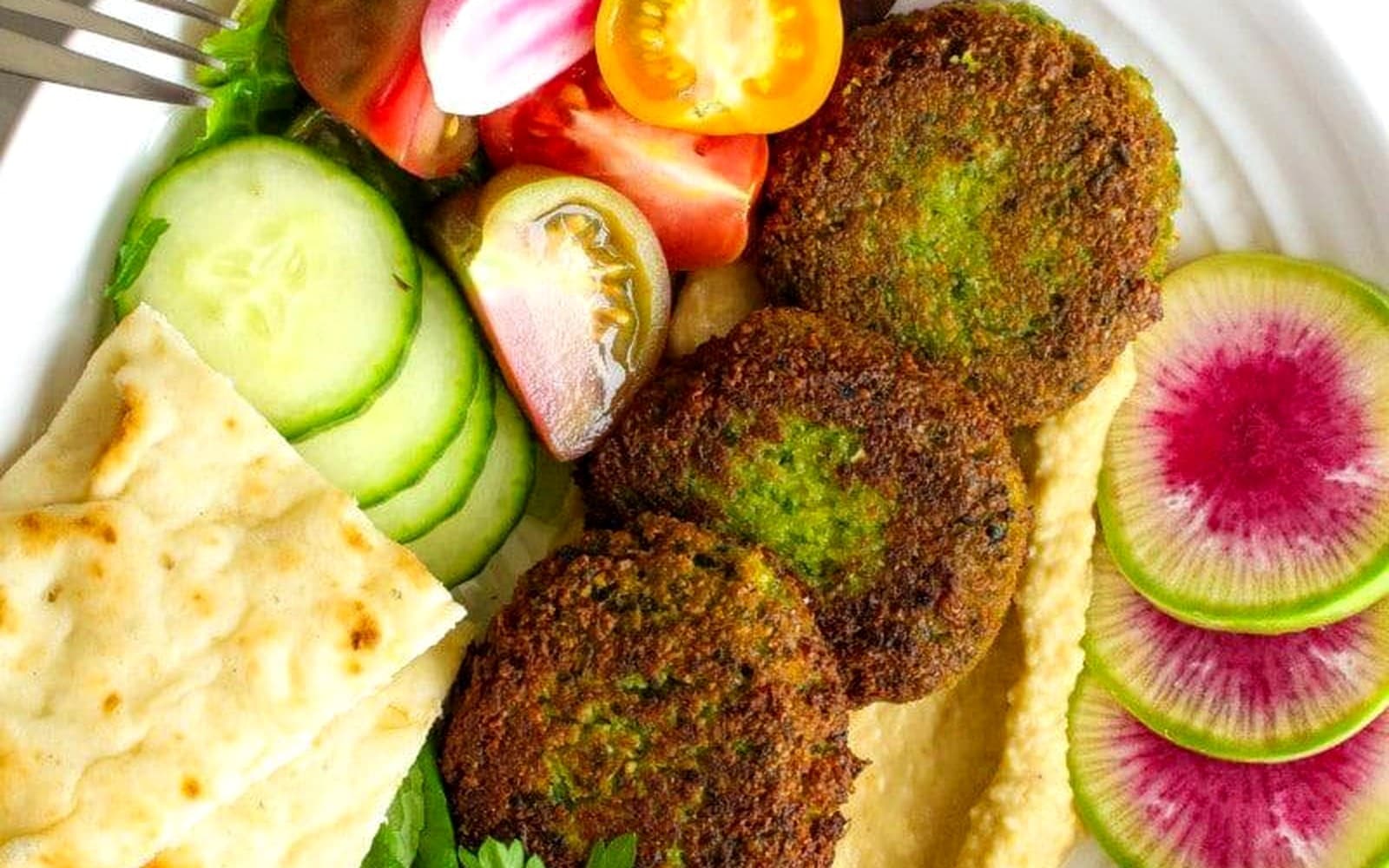 A premium falafel plate with hummus, cucumber, radish, herbs, and pita