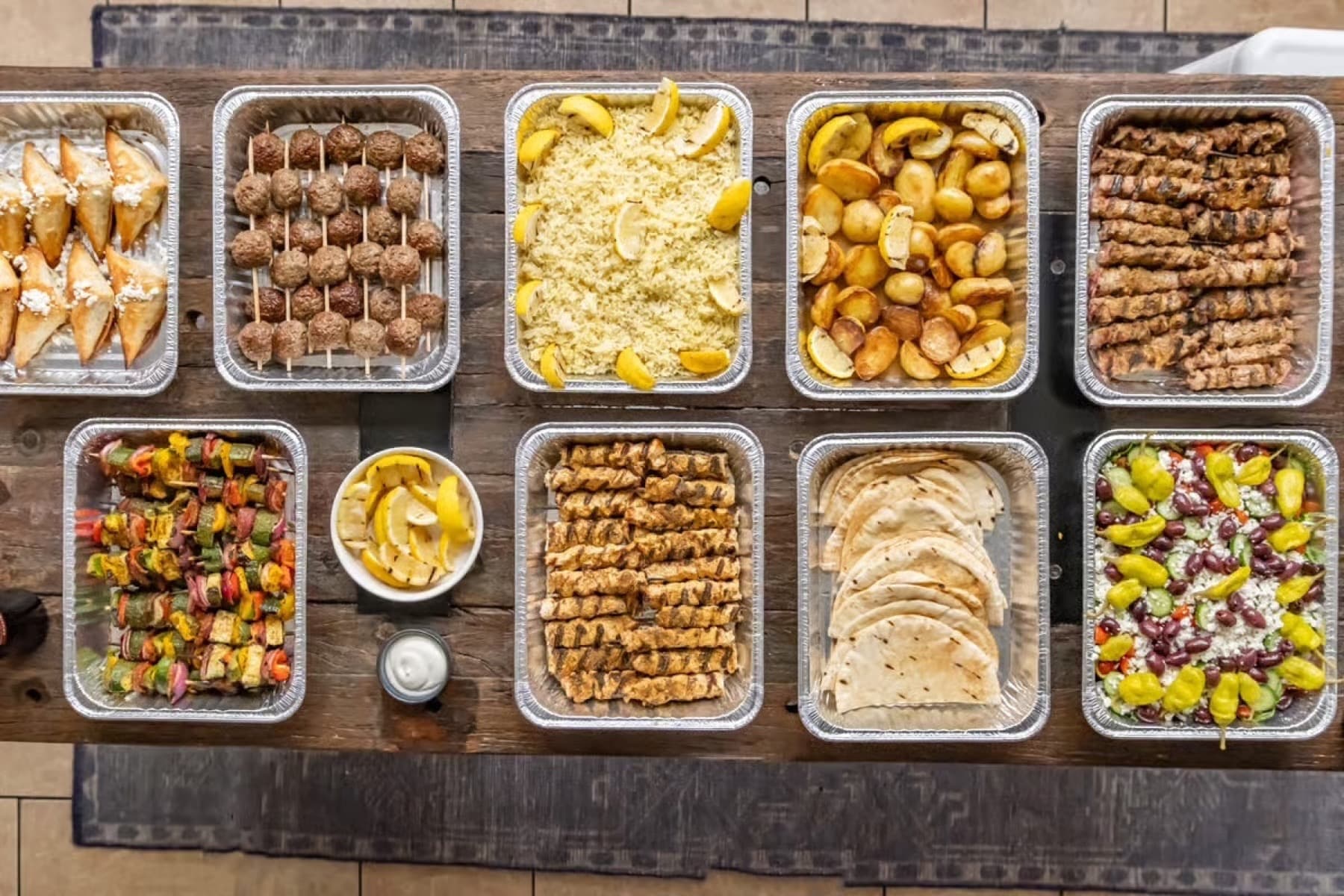 Full catering spread with souvlaki, rice, potatoes, Greek salad, pita, and sides